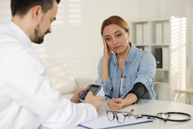 Cardiologist measuring patient's blood pressure at table in hospital