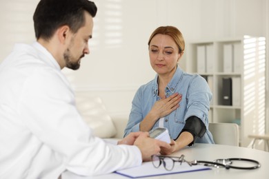 Photo of Cardiologist measuring patient's blood pressure at table in hospital