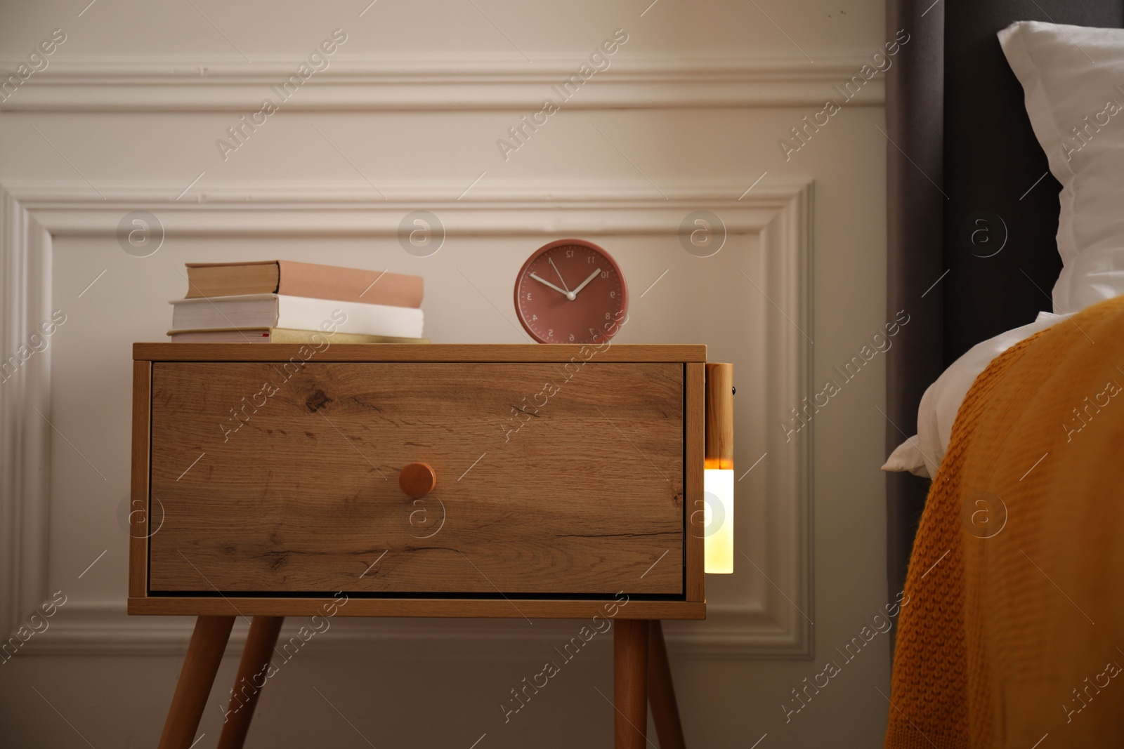 Photo of Glowing modern LED lamp on wooden bedside table indoors