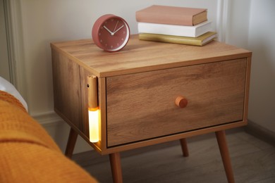 Photo of Glowing modern LED lamp on wooden bedside table indoors