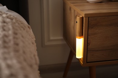 Photo of Glowing modern LED lamp on wooden bedside table indoors, closeup