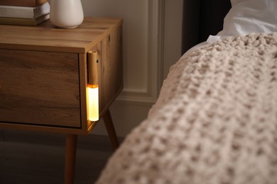 Photo of Glowing modern LED lamp on wooden bedside table indoors, closeup