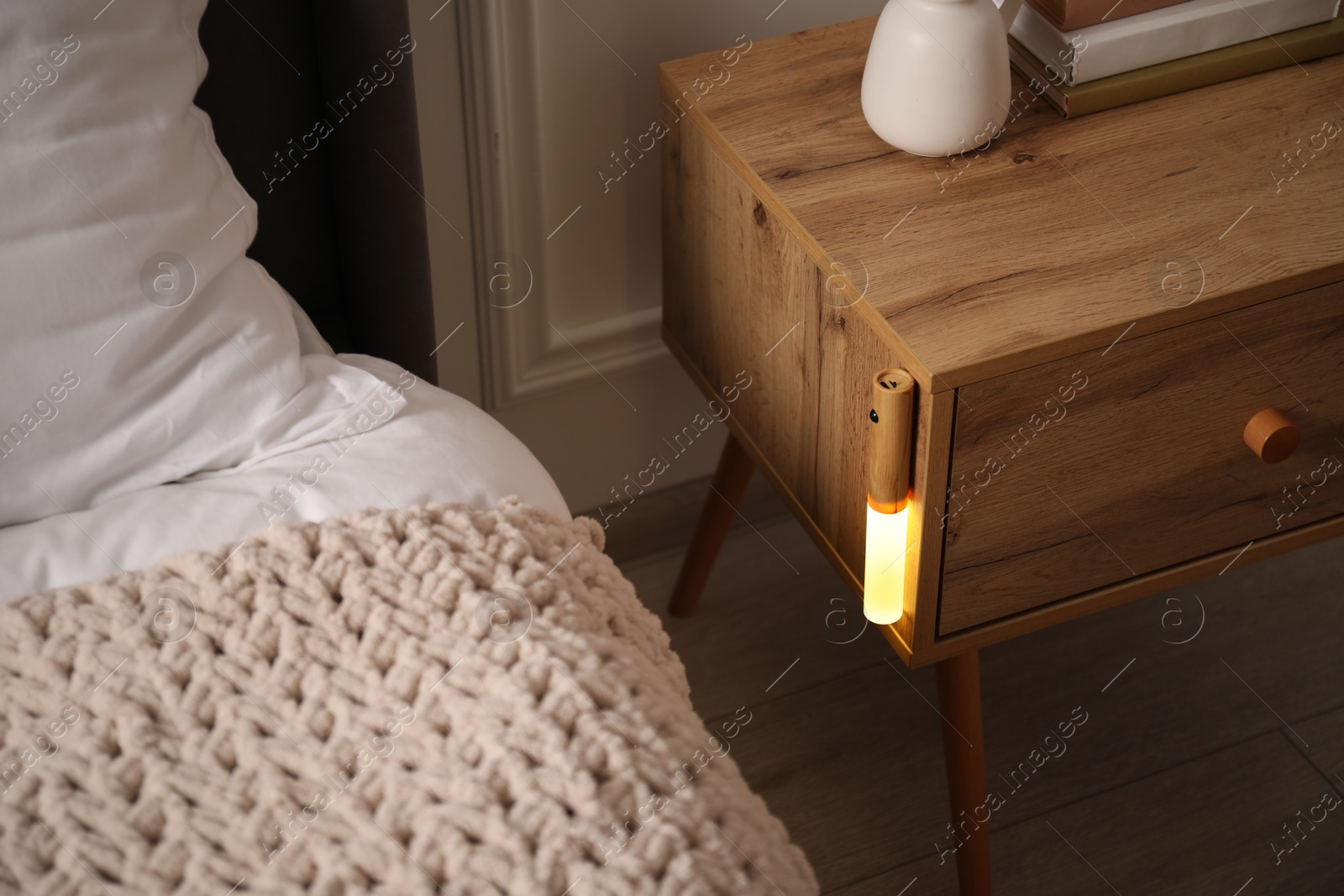 Photo of Glowing modern LED lamp on wooden bedside table indoors