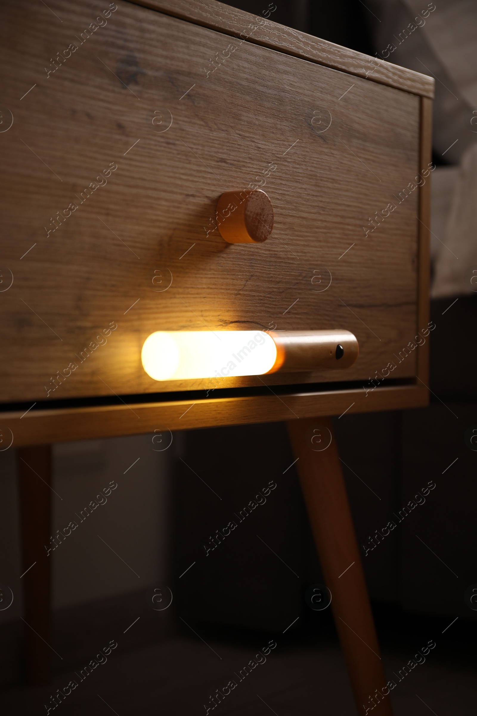 Photo of Glowing modern LED lamp on wooden bedside table indoors, closeup