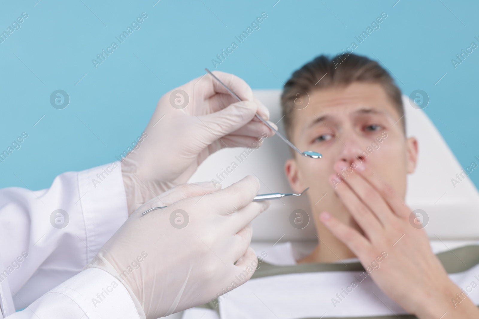 Photo of Scared man having appointment with dentist on light blue background, selective focus