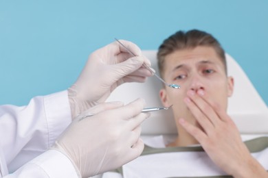 Scared man having appointment with dentist on light blue background, selective focus