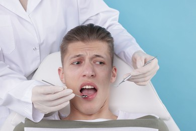 Photo of Scared man having appointment with dentist on light blue background