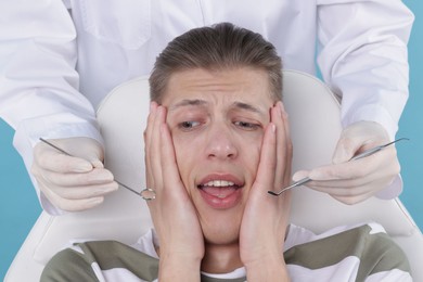 Photo of Scared man having appointment with dentist on light blue background