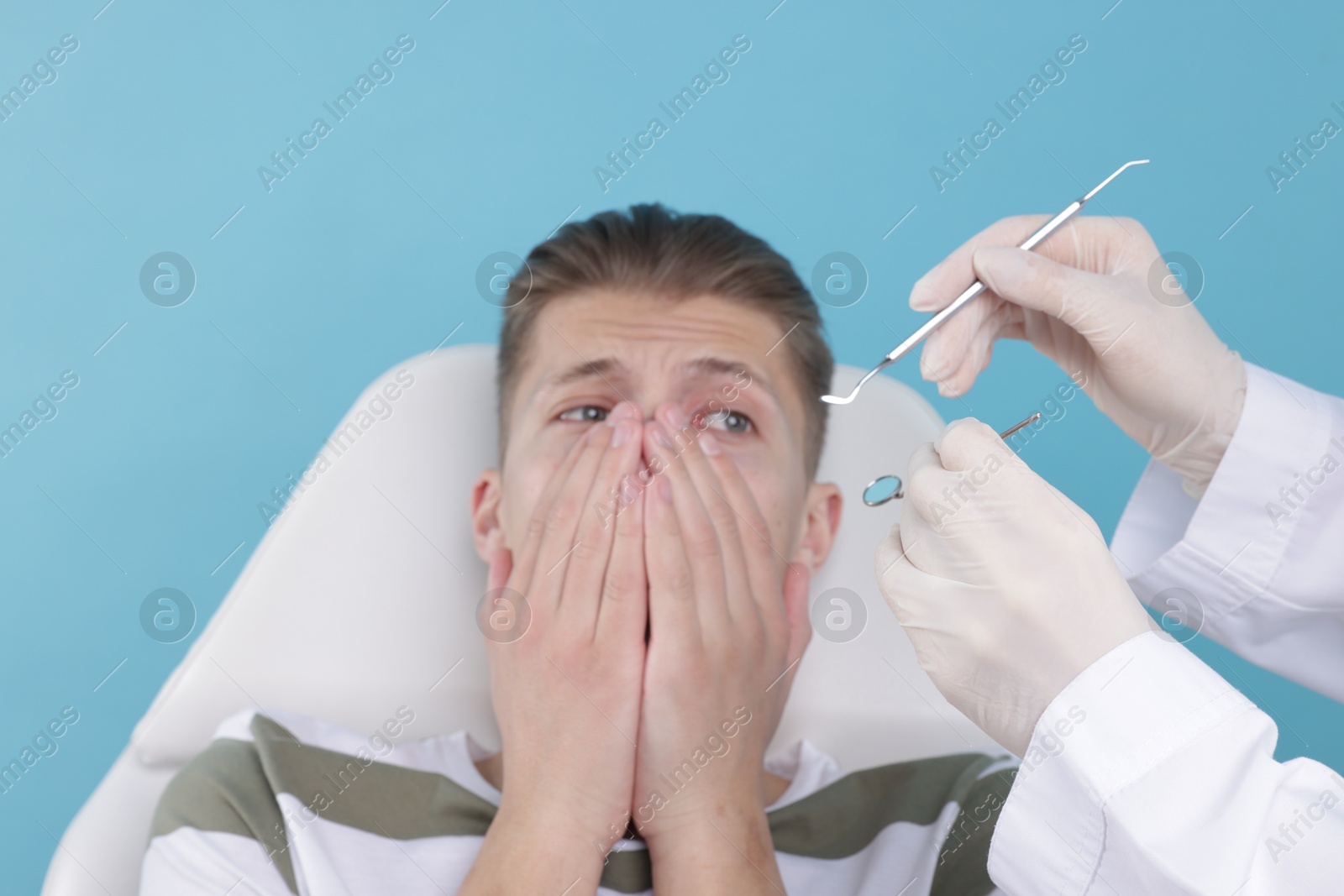 Photo of Scared man covering mouth and dentist with tools on light blue background