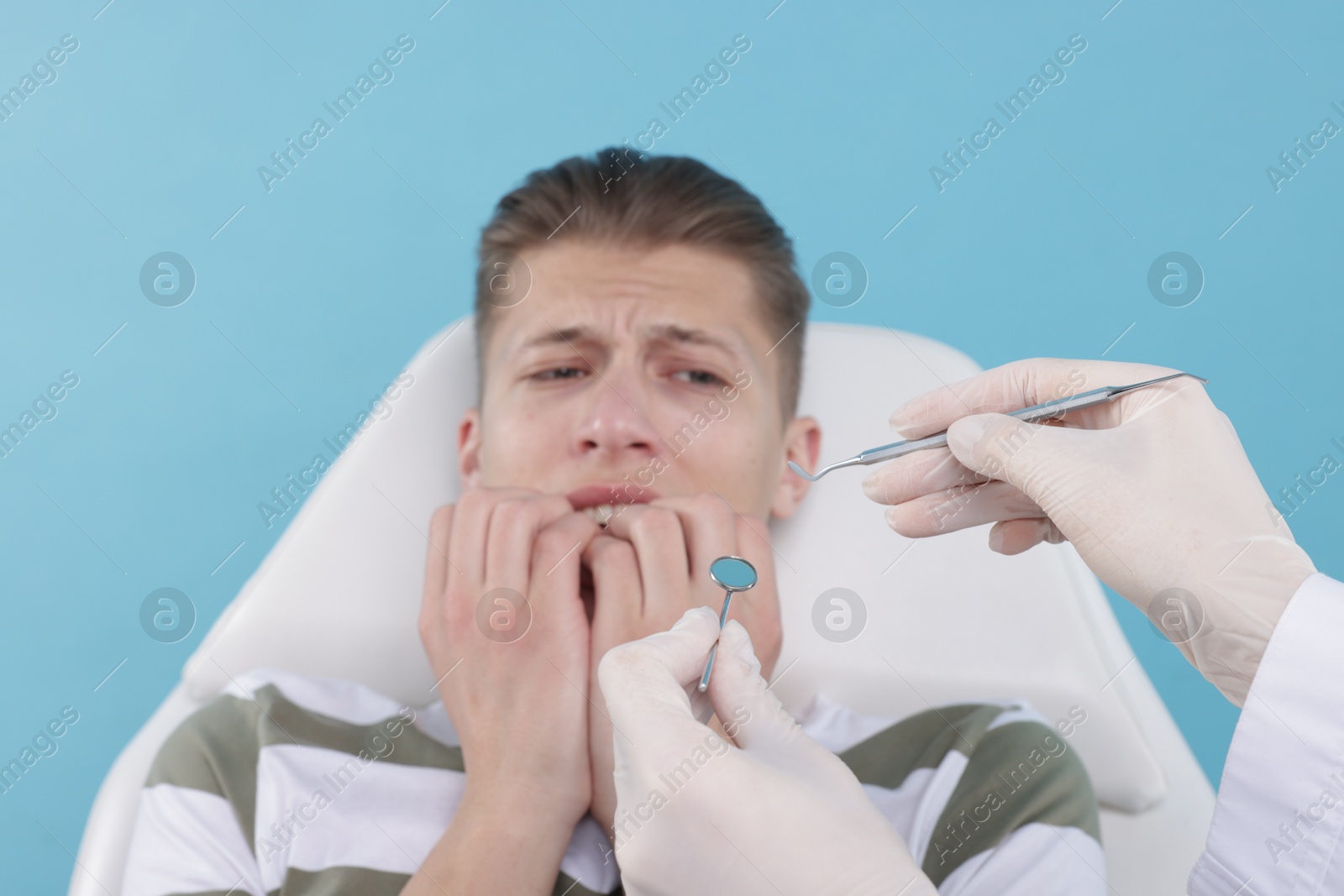 Photo of Scared man having appointment with dentist on light blue background