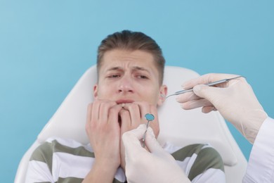 Photo of Scared man having appointment with dentist on light blue background