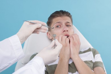 Photo of Scared man having appointment with dentist on light blue background