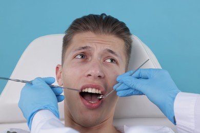 Photo of Scared man having appointment with dentist on light blue background