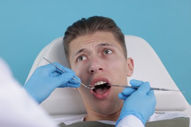 Scared man having appointment with dentist on light blue background