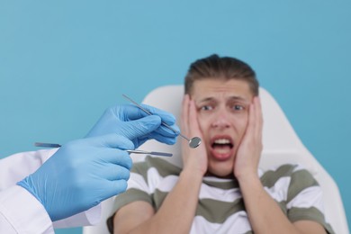 Photo of Scared man having appointment with dentist on light blue background, selective focus