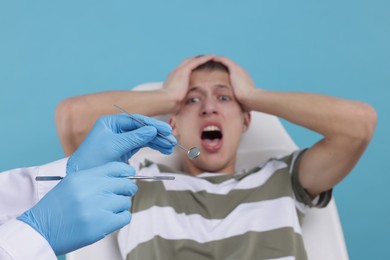 Scared man having appointment with dentist on light blue background, selective focus