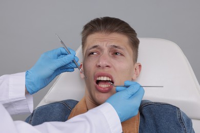 Scared man having appointment with dentist on grey background