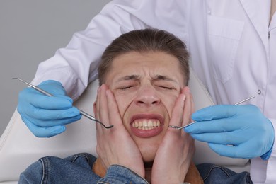 Scared man having appointment with dentist on grey background