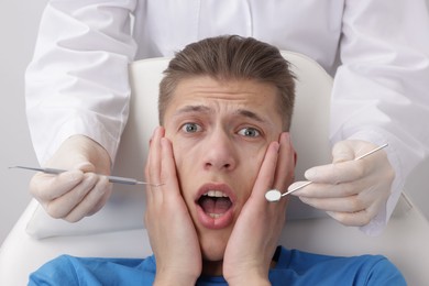 Scared man having appointment with dentist on grey background