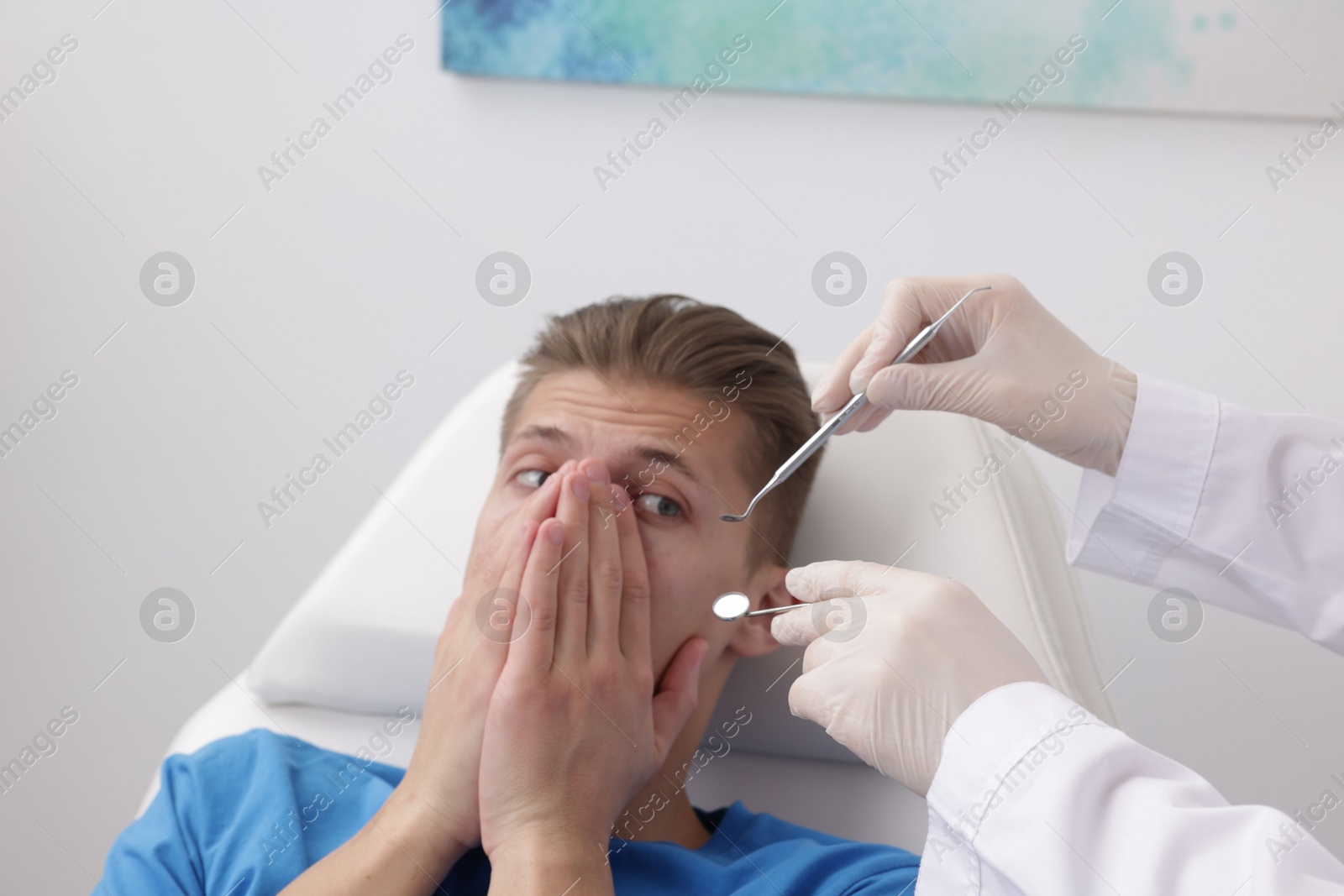 Photo of Scared man covering mouth and dentist with tools in clinic