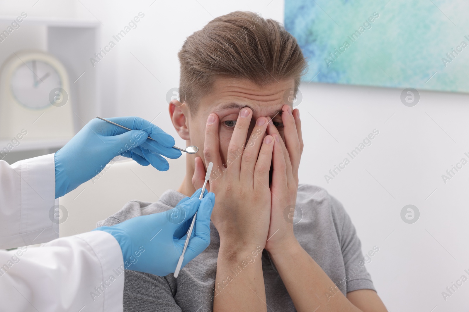 Photo of Scared man covering face and dentist with tools in clinic