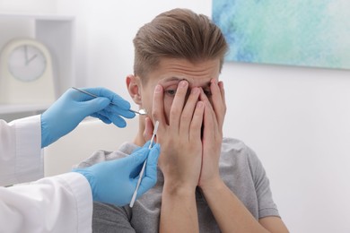 Photo of Scared man covering face and dentist with tools in clinic