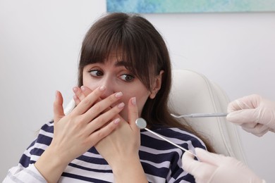 Scared woman covering mouth and dentist with tools in clinic