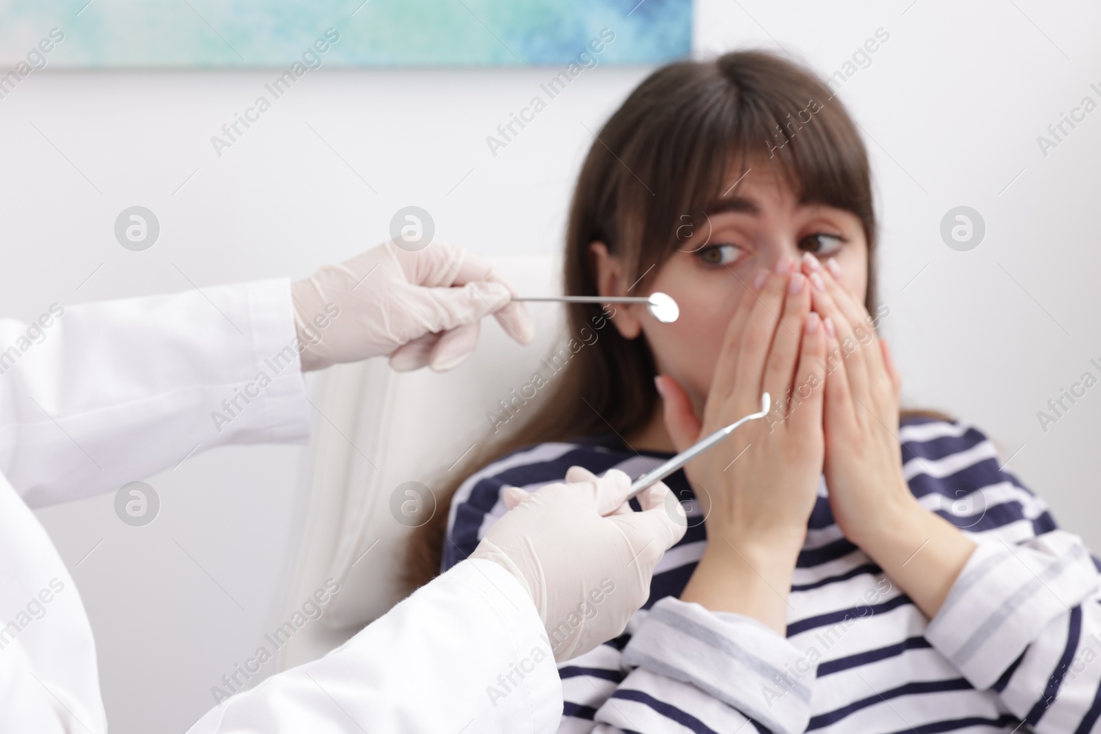 Photo of Scared woman covering mouth and dentist with tools in clinic, selective focus