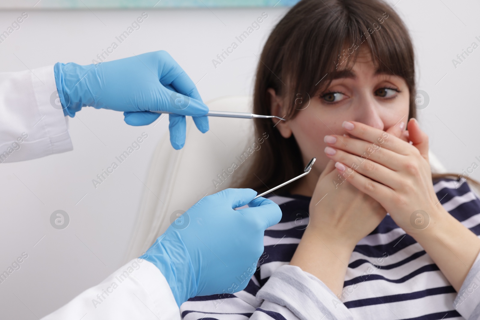 Photo of Scared woman covering mouth and dentist with tools in clinic