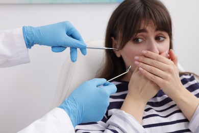 Photo of Scared woman covering mouth and dentist with tools in clinic