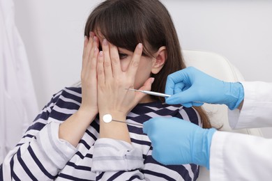 Photo of Scared woman covering face and dentist with tools in clinic