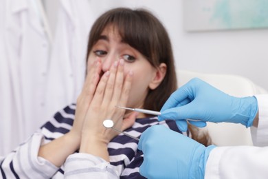 Scared woman covering mouth and dentist with tools in clinic, selective focus