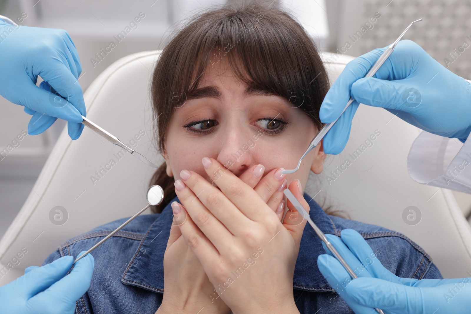 Photo of Scared woman having appointment with dentist and assistant in clinic