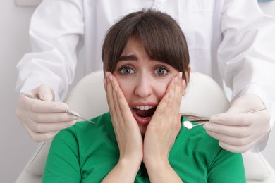 Scared woman having appointment with dentist on grey background