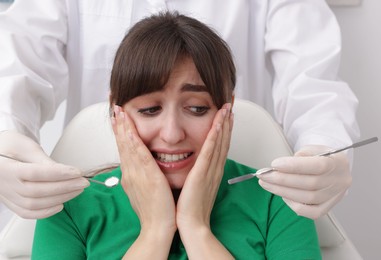 Scared woman having appointment with dentist on grey background