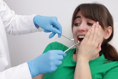 Scared woman having appointment with dentist on grey background