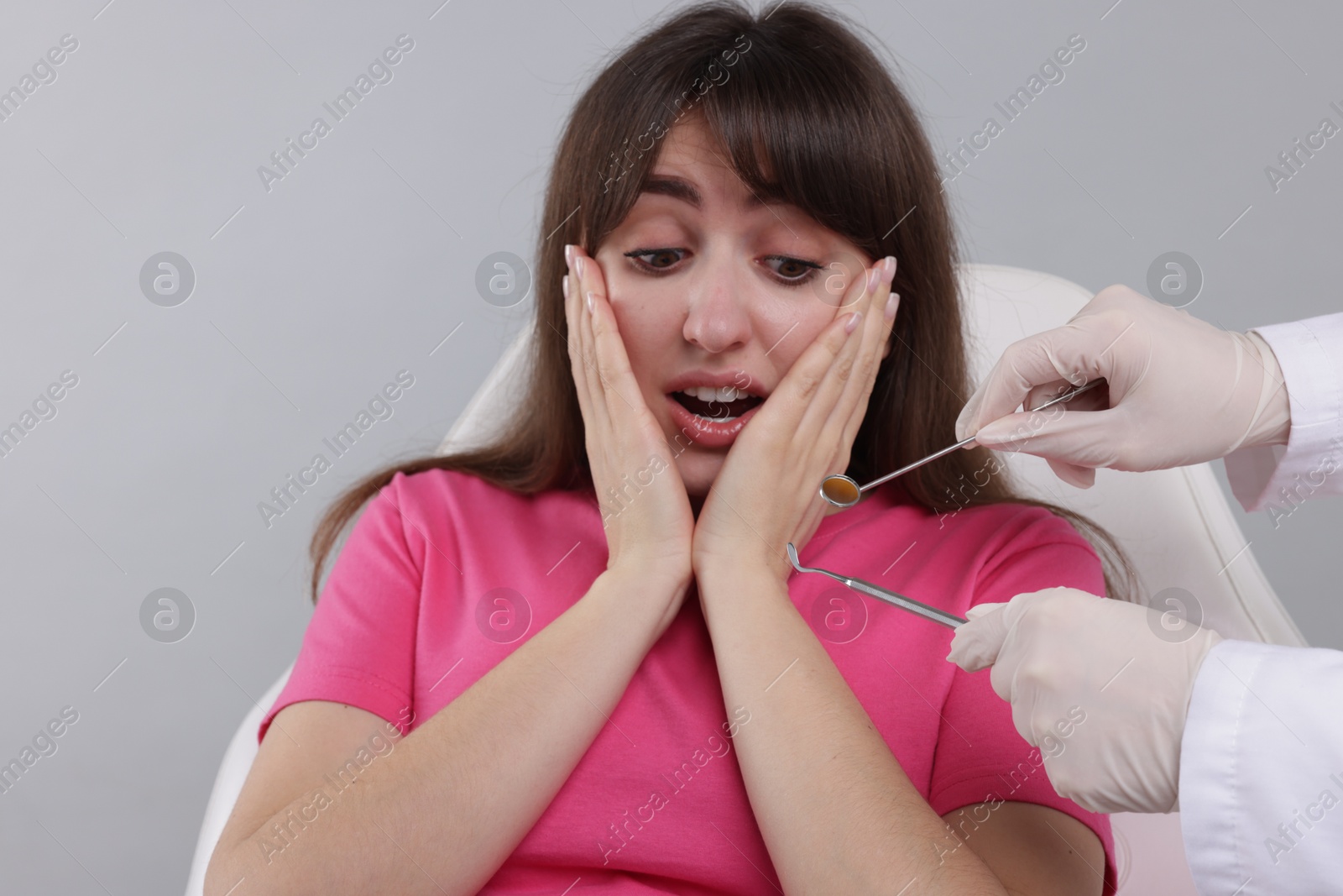 Photo of Scared woman having appointment with dentist on grey background