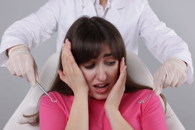 Scared woman having appointment with dentist on grey background