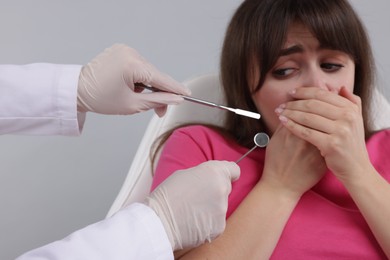 Scared woman covering mouth and dentist with tools on grey background