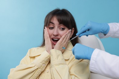 Scared woman having appointment with dentist on light blue background