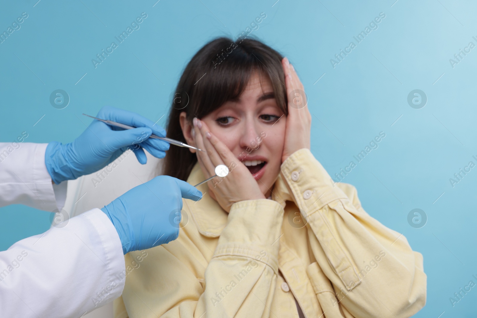 Photo of Scared woman having appointment with dentist on light blue background