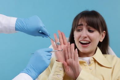 Photo of Scared woman refusing dentist's examining on light blue background