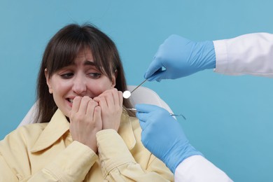 Scared woman having appointment with dentist on light blue background