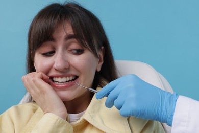 Scared woman having appointment with dentist on light blue background