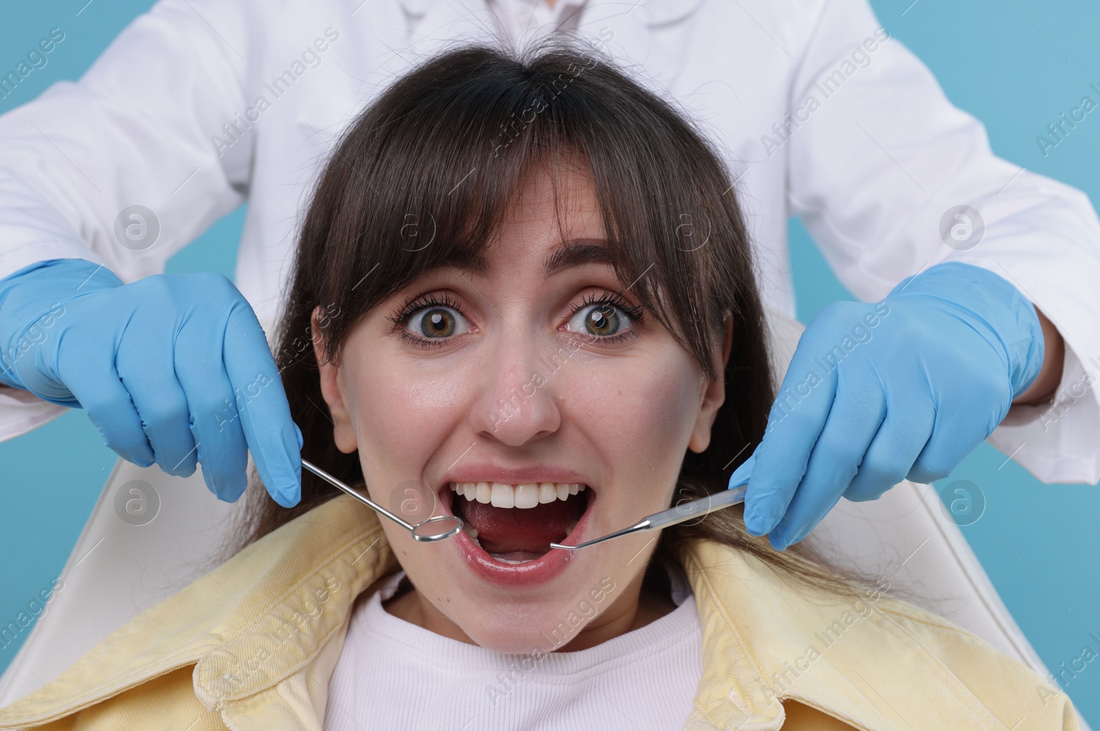 Photo of Scared woman having appointment with dentist on light blue background