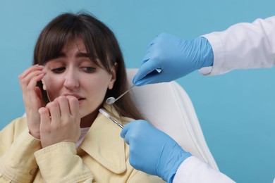 Scared woman having appointment with dentist on light blue background