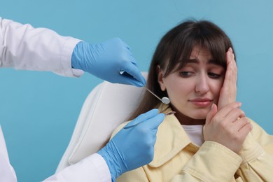 Scared woman having appointment with dentist on light blue background