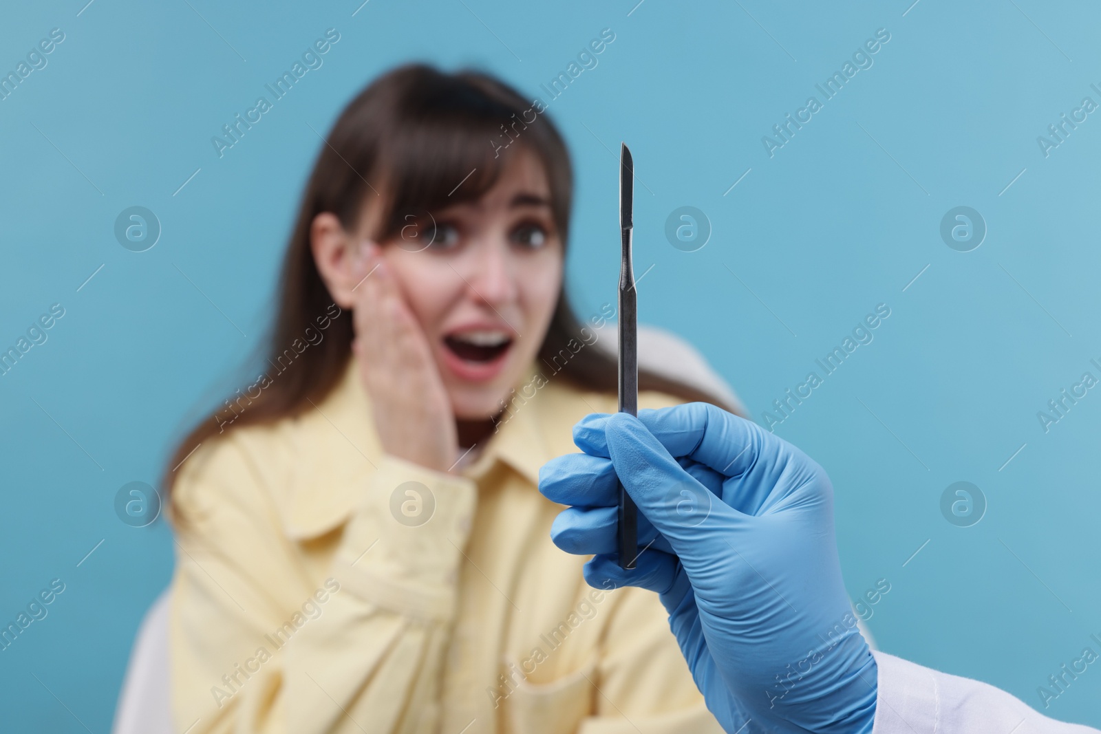 Photo of Scared woman having appointment with dentist on light blue background, selective focus