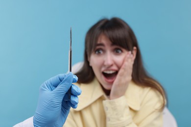 Scared woman having appointment with dentist on light blue background, selective focus