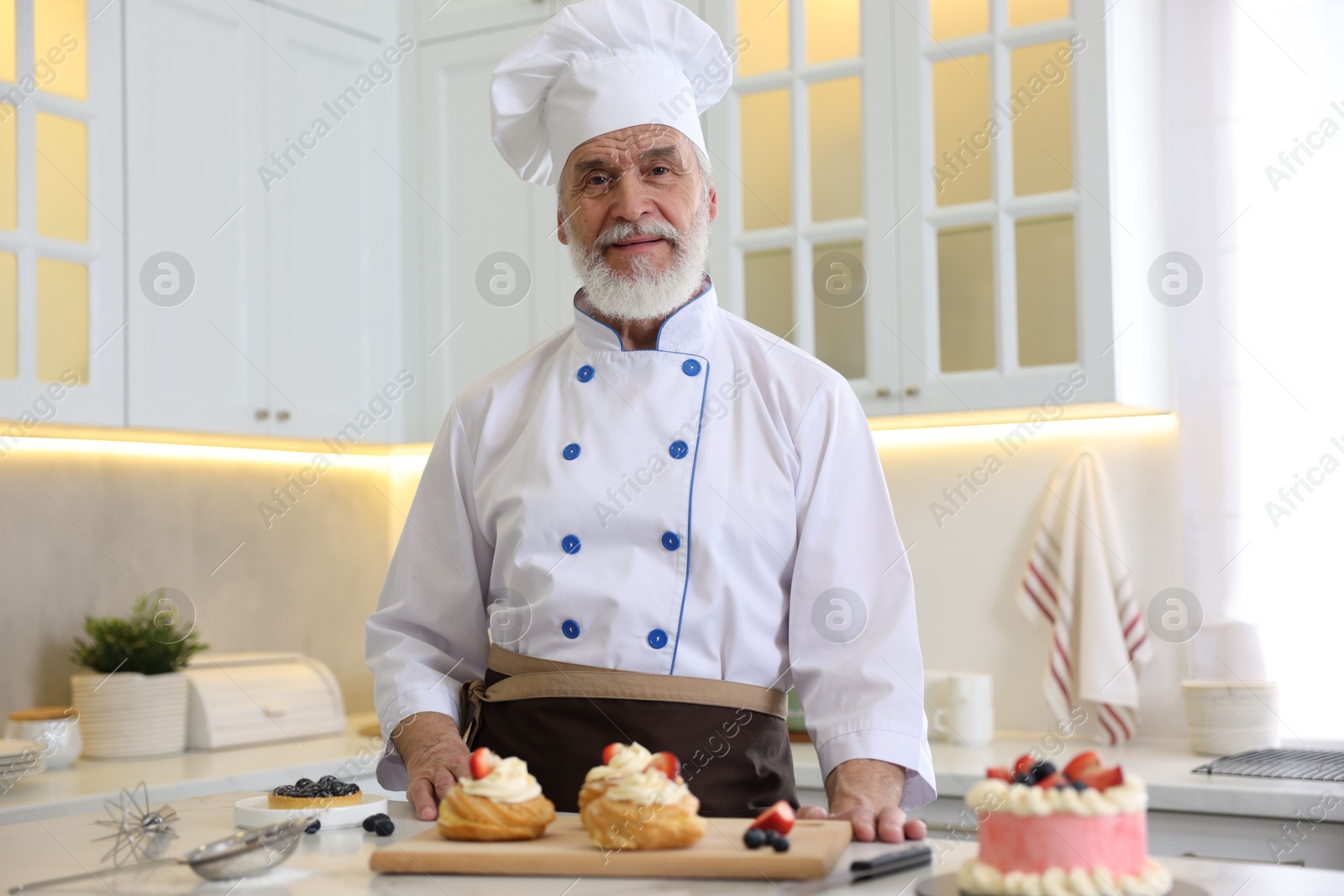 Photo of Elderly pastry chef at table with desserts in kitchen